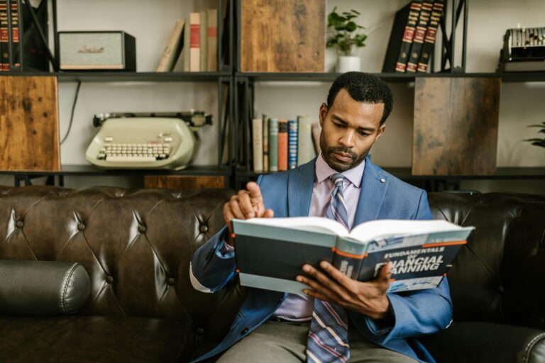 Focused businessman in a suit reading a financial planning book in office setting.